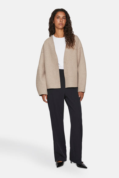 Beige jas van VILA® met lange mouwen, gedragen met een wit T-shirt en zwarte broek.