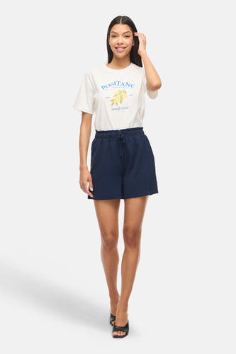 Donkerblauwe short van VILA® met hoge elastische taille en trekkoord, van gestructureerde stof. Gedragen met wit T-shirt en zwarte sandalen.