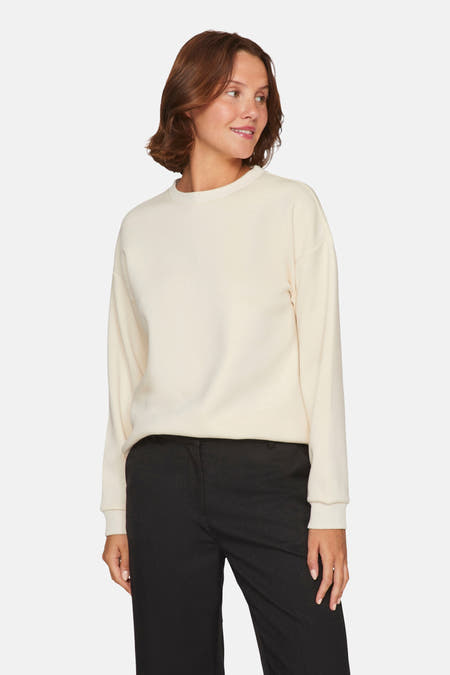 Beige sweater van VILA®, gedragen met zwarte pantalon, staand op een witte achtergrond.
