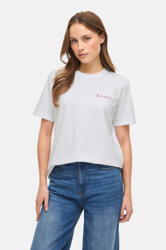 T-shirt blanc à manches courtes de VILA®, avec une bordure rouge "amore" et porté avec des jeans bleus décontractés et des sandales noires à talon.
