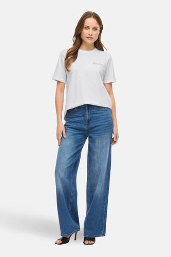 Wit T-shirt met korte mouwen van VILA®, met rode "amore" borduring en gedragen met blauwe wijde pijpen jeans en zwarte sandalen met hak.
