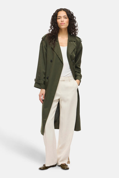 Groene lange jas van VILA®, gedragen met een wit topje en beige broek.
