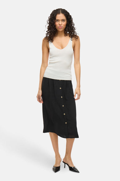 Blouse blanche sans manches de VILA, portée avec une jupe noire à carreaux et des bottines noires.