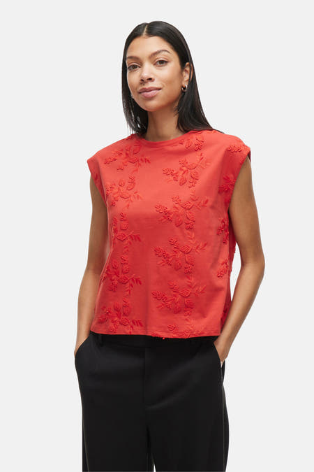 T-shirt sans manches rouge de VILA® avec des motifs floraux brodés, associé à un pantalon noir.