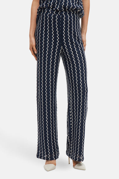 Pantalon bleu de VILA, avec des motifs zigzag blancs et des strass, associé à des escarpins blancs.