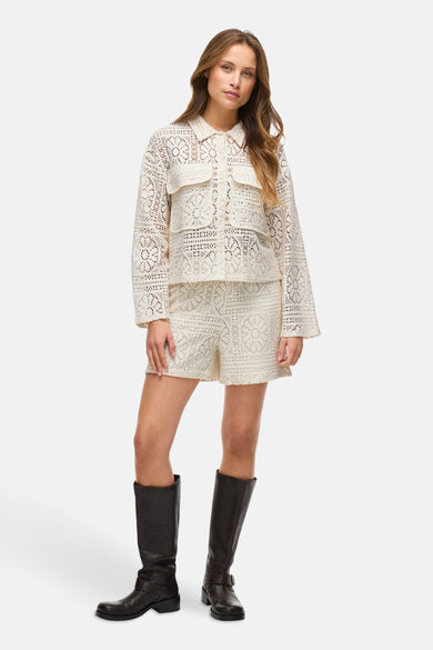 Ecru hemd met lange mouwen van VILA®, met openwork details en gedragen met bijpassende shorts en zwarte laarzen.
