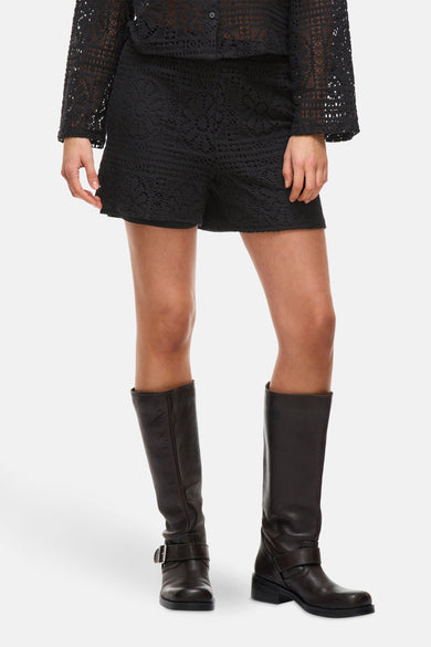 Zwarte short van VILA met open details, gecombineerd met een gebreid, zwart bovenstuk en leren laarzen.
