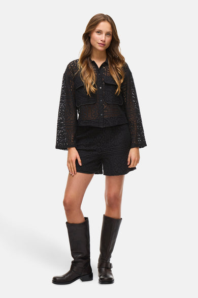 Zwarte short van VILA, met opengewerkt kanten patroon, gecombineerd met laarzen en een bijpassende blouse.
