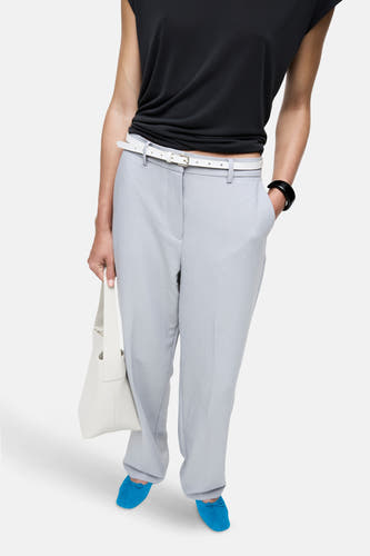 Grijze broek van VILA®, gedragen met een witte riem, zwarte top en blauwe schoenen, en een witte handtas.