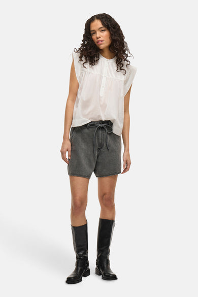 Grijze short van VILA met een strikceintuur en gedragen met zwarte laarzen en een witte blouse.
