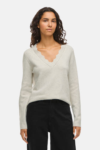 Gilet V-hals beige de VILA®, avec des détails décoratifs le long de la ligne du col, associé à un pantalon noir.