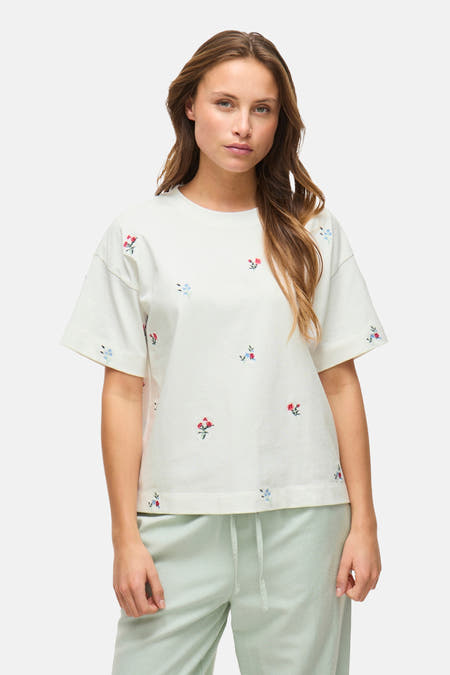 Wit T-shirt met korte mouwen van VILA®, met bloemenborduursel, gedragen met een groene joggingbroek.
