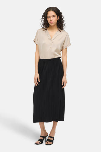 Blouse beige à manches courtes de VILA®, portée avec une jupe plissée noire et des talons noirs.