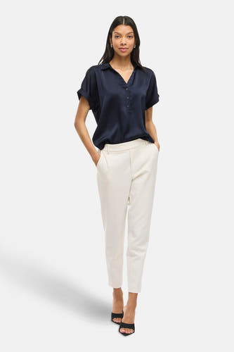 Blauwe blouse met korte mouwen van VILA, met een knoopsluiting en gedragen met een witte pantalon.