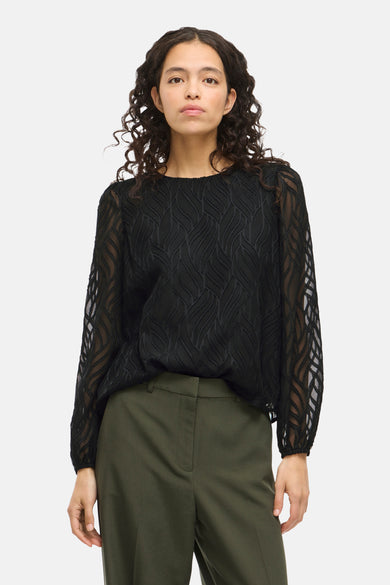 Blouse noire à manches longues de VILA®, avec un motif subtilement ondulé et associée à une pantalon vert.