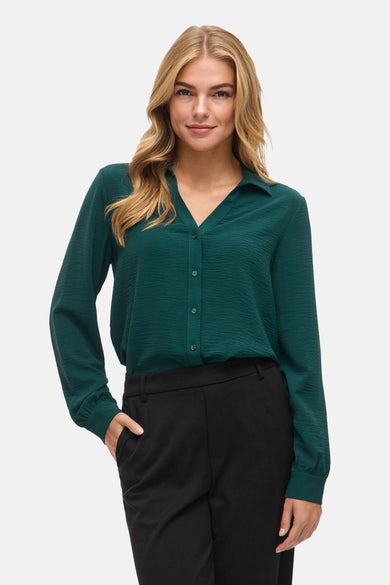 Blouse verte avec manches longues de VILA®, à collier et portée avec un pantalon noir et des talons.