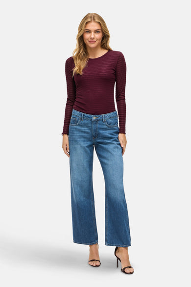 Paars T-shirt met lange mouwen van VILA, gedragen met blauwe wijde pijpen jeans en zwarte hakken.
