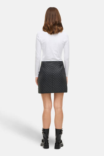 Zwarte korte rok van VILA, met gewatteerd ruitpatroon, gecombineerd met een wit shirt met lange mouwen en zwarte laarzen.