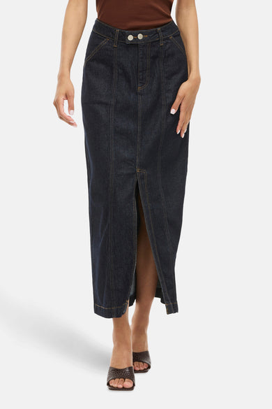 Lange rok van donkerblauw denim van VILA, met split aan de voorkant en bruine sandalen.
