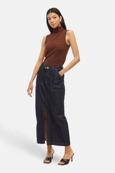 Lange rok in donkerblauw denim van VILA, met een split aan de voorkant, gecombineerd met een bruine top en hakken.
