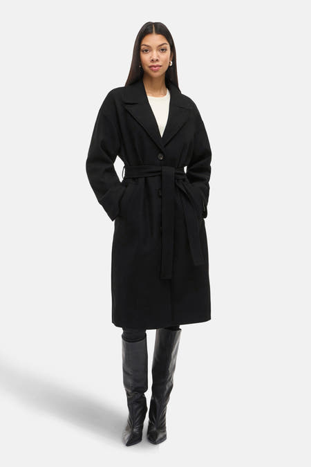 Manteau long noir de VILA®, avec ceinture et bottes noires en cuir.