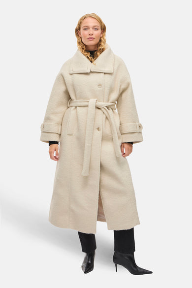 Blanc cassé long manteau de VILA®, avec une ceinture, des manches longues et porté sur du noir et des bottes.