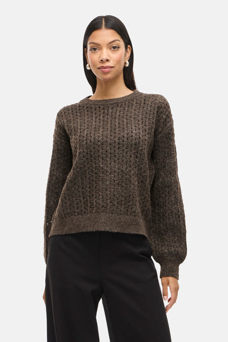 Bruine trui met ronde hals van VILA, met een grof gebreide textuur, gedragen met een zwarte broek.
