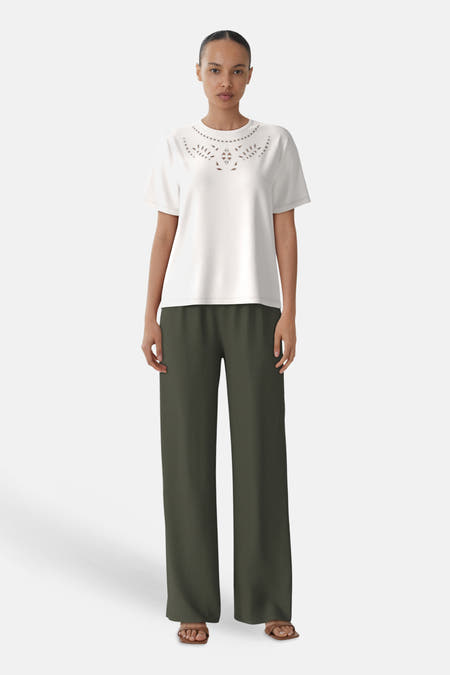 T-shirt blanc à manches courtes de VILA®, avec des découpes décoratives autour de la ligne du col, associé à un pantalon kaki et des sandales.