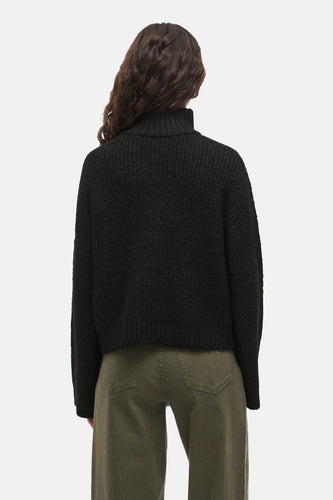 Zwarte trui van VILA, gezien van achteren, met een hoge kraag en geribbelde textuur, gecombineerd met een groene broek.
