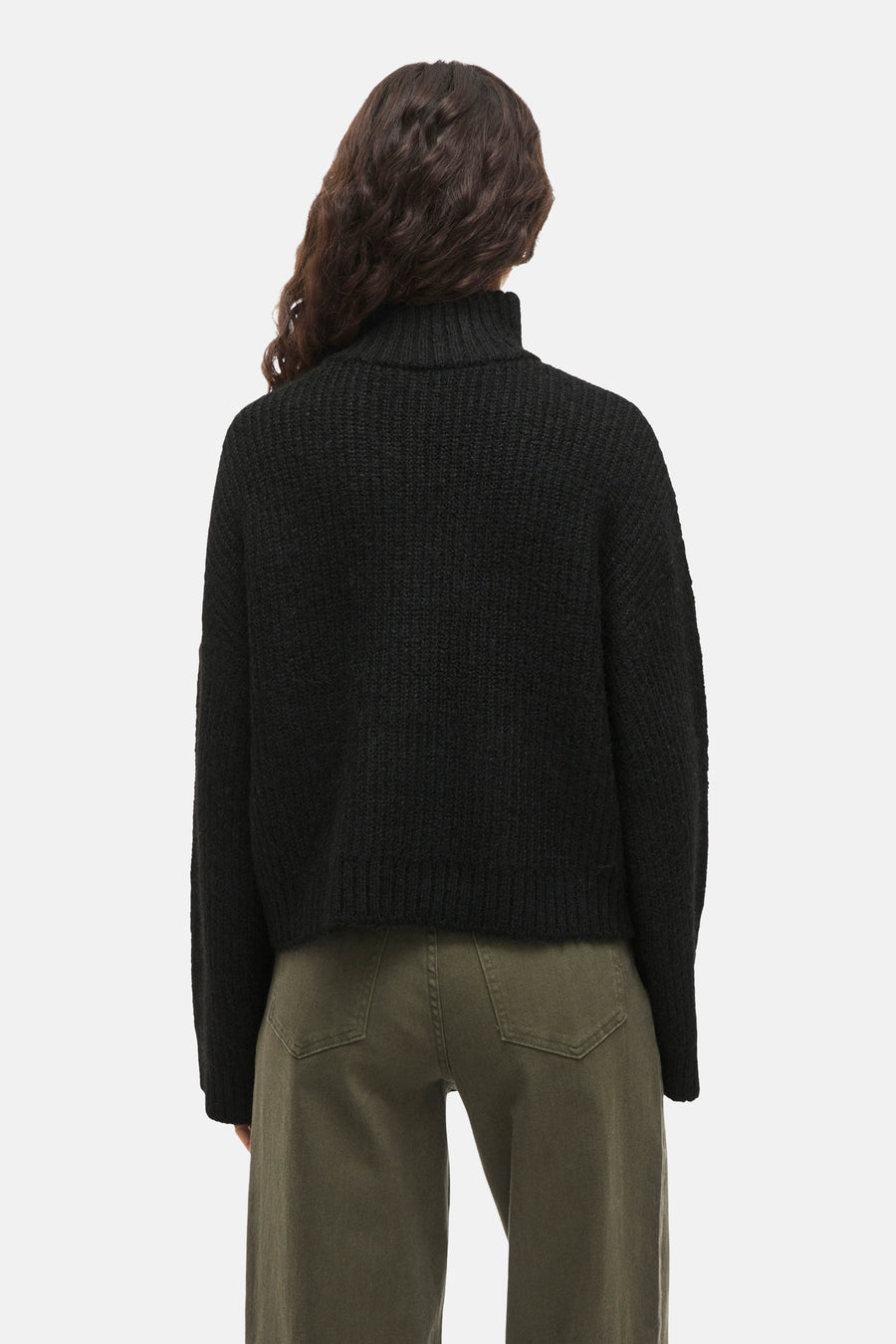 Zwarte trui van VILA, gezien van achteren, met een hoge kraag en geribbelde textuur, gecombineerd met een groene broek.
