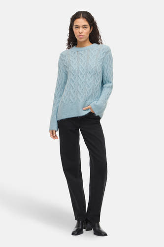 Blauwe trui met ronde hals van VILA®, kabelpatroon en gedragen met zwarte jeans en enkellaarsjes.
