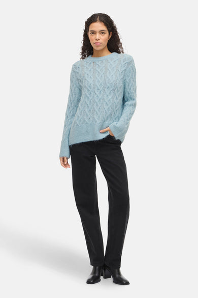 Blauwe trui met ronde hals van VILA®, kabelpatroon en gedragen met zwarte jeans en enkellaarsjes.
