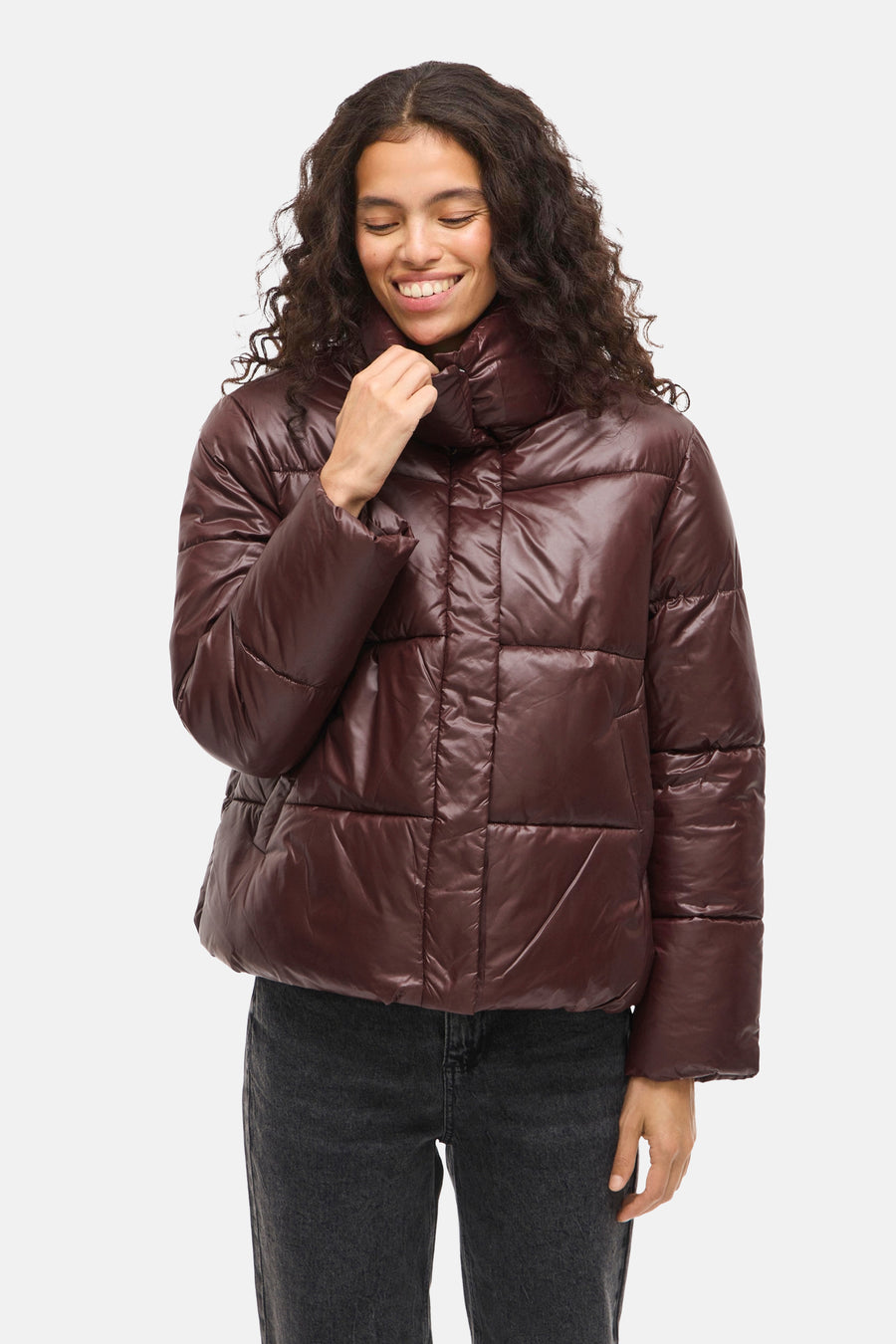 Vrouw met bruine pufferjas en zwarte jeans.
