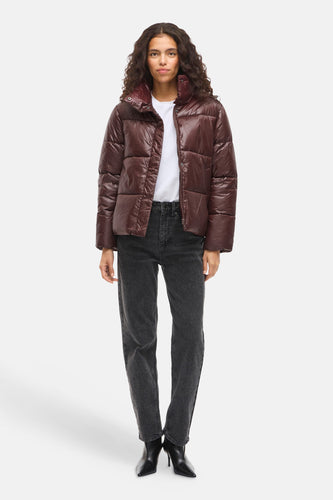 Vrouw met bruine pufferjas, grijze jeans en zwarte hakken.