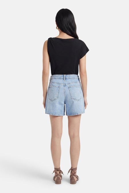 Lichtblauwe denim short van VILA, getoond vanaf de achterkant, gedragen met een zwarte top en bruine sandalen.