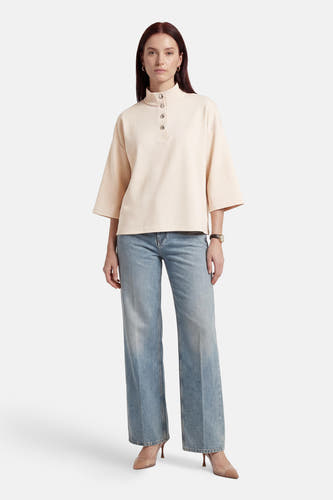 Beige sweater van VILA®, met een knoopsluiting en wijde mouwen, gecombineerd met een blauwe jeans en hoge hakken.
