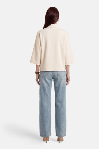 Beige sweater van VILA®, met driekwart mouwen en een hoge kraag, gecombineerd met lichtblauwe jeans en hakken.