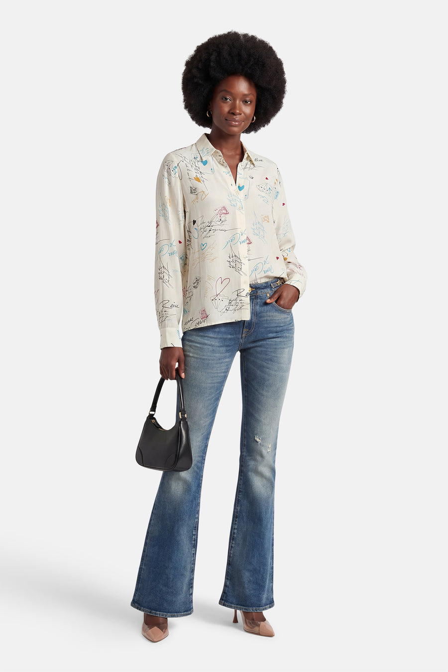 Multikleurig overhemd met lange mouwen van VILA, versierd met speelse illustraties en gedragen met blauwe jeans en een zwarte tas.
