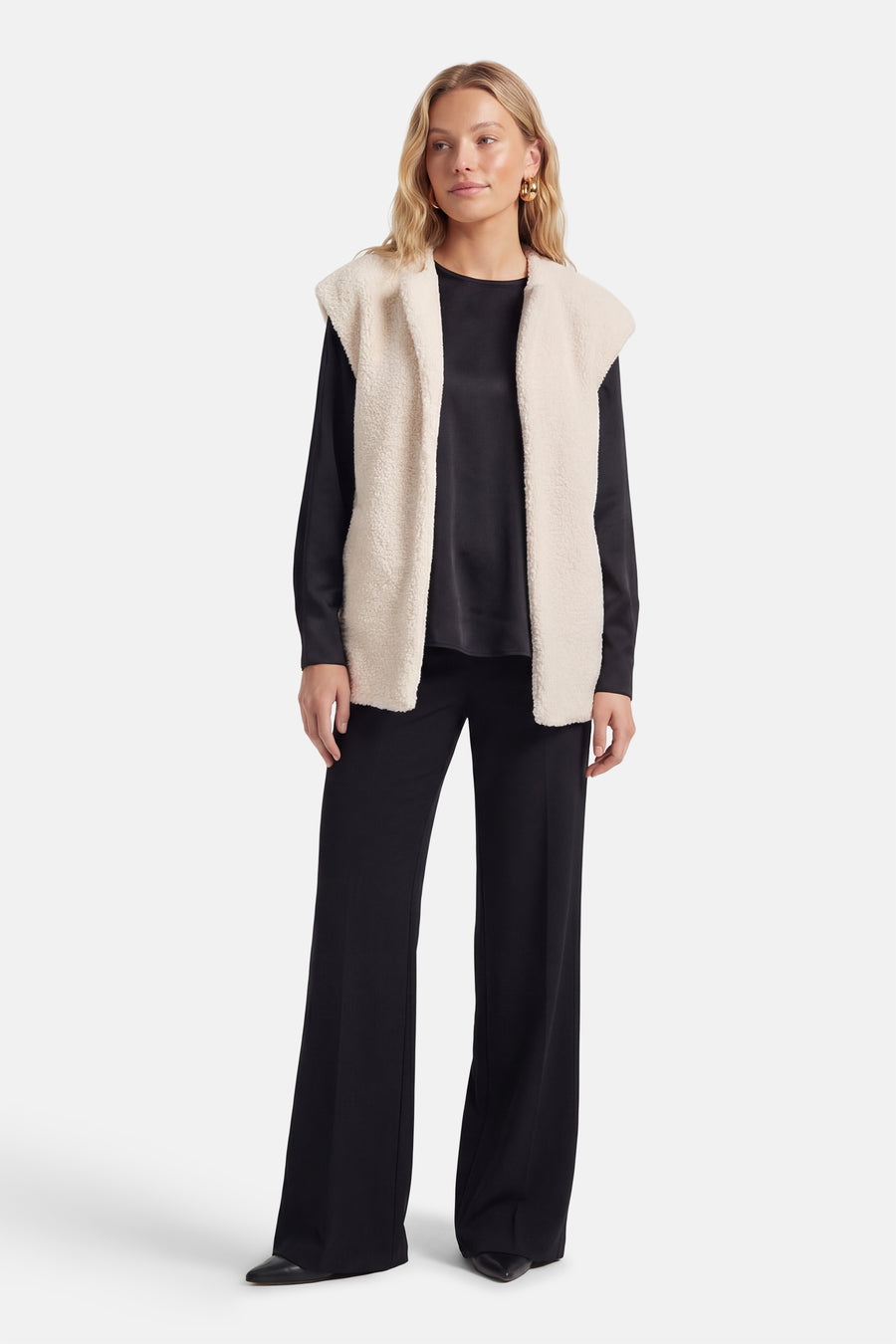 Manteau beige de VILA®, porté sur un haut noir et un pantalon, avec des boucles d'oreilles dorées.