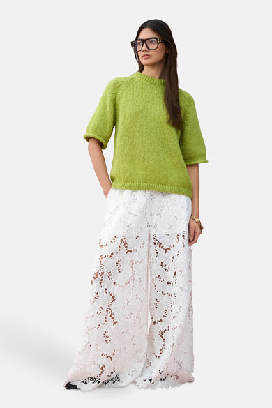 Pantalon blanc de VILA® avec imprimé floral et larges bretelles, associé à une chemise verte et un bracelet doré.