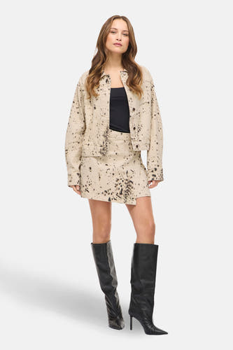 Korte beige rok van VILA, met een donkerbruin vlekkenpatroon en asymmetrische snit, gedragen met zwarte laarzen.
