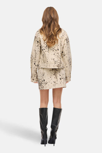 Beige korte rok van VILA, met een abstract zwart stippenpatroon, gecombineerd met zwarte kniehoge laarzen.
