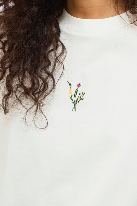 Wit T-shirt van VILA®, met korte mouwen en een kleine geborduurde bloem op de borst.