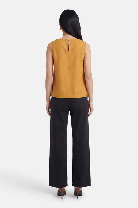 Achterkant van mouwloze gele blouse van VILA® met keyhole-uitsnijding in de nek en strikjes aan de zijkanten, gedragen met zwarte jeans en hakken.