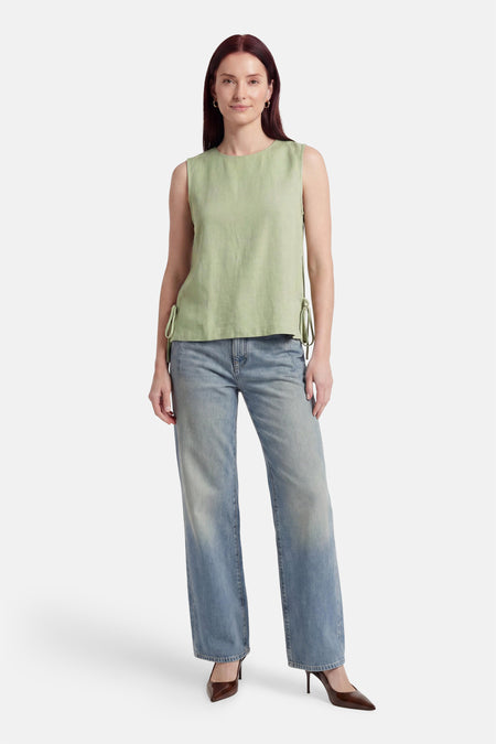 Groene mouwloze blouse van VILA® met trekkoorden aan de zijkant, gecombineerd met lichtblauwe jeans en bruine hakken.