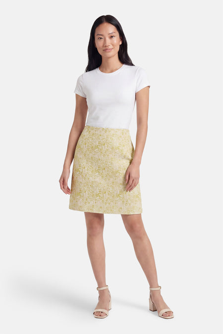 Jupe courte verte de VILA® avec un motif floral subtil, portée par un mannequin avec un t-shirt blanc et des sandales.