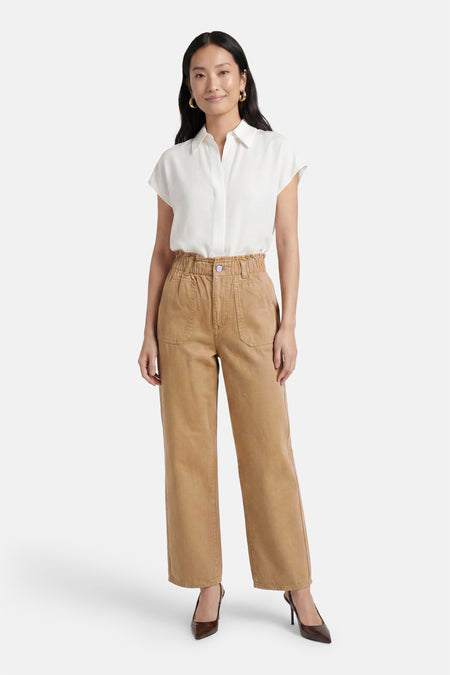 Bruine broek van VILA® met hoge paperbag taille, paarse knoop, opgestikte zakken en wijde pijpen, gestyled met een wit overhemd en donkerbruine hakken.