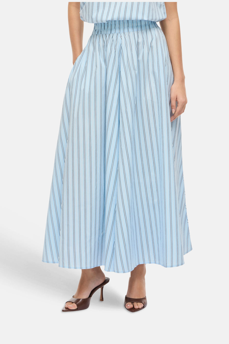 Jupe longue bleue à rayures de VILA®, avec une taille élastique et des poches latérales, portée avec des mules marron.