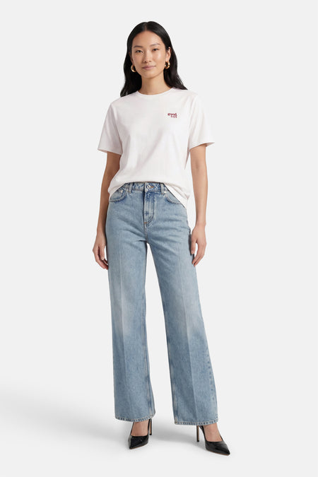 Wit T-shirt met korte mouwen van VILA®, met kleine rode tekstprint, gedragen met wijde jeans en zwarte pumps.