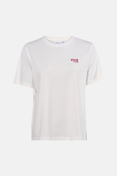 T-shirt blanc à manches courtes de VILA®, avec petit imprimé texte rouge, porté avec un jean ample et des escarpins noirs.